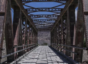تصویر یک پل قدیمی فلزی و چوبی به سمت کوه