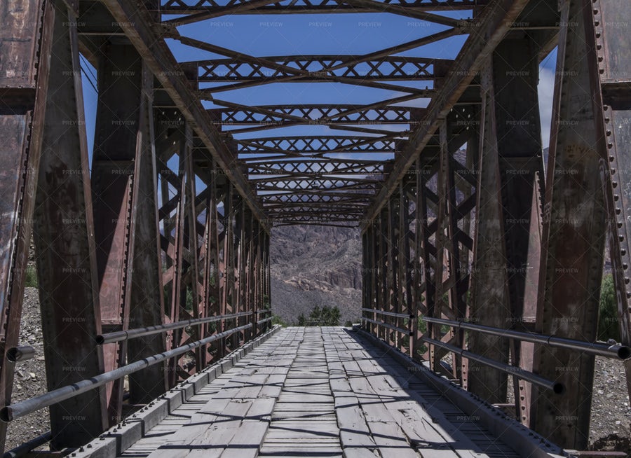 تصویر یک پل قدیمی فلزی و چوبی به سمت کوه