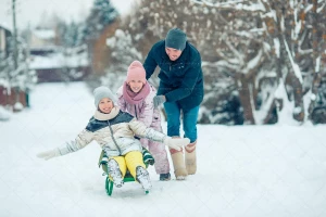 دو دختر کوچک در حال سورتمه سواری با کمک پدر