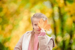 دختره بچه‌ای که صورتش را با یک برگ افرا پوشانده است