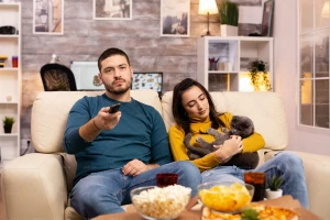 زوج جوان درحال نگاه کردن تلویزیون و خوردن غذای ناسالم