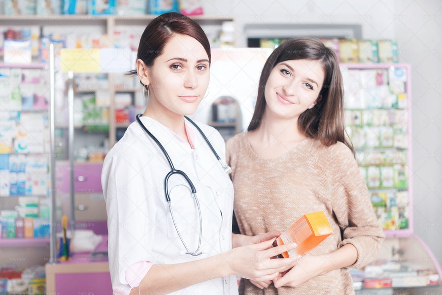 تصویر یک دکتر در داروخانه که یک بسته دارو در دست دارد