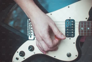 دست یک نفر که با پیک در حال نواختن گیتار الکتریک است
