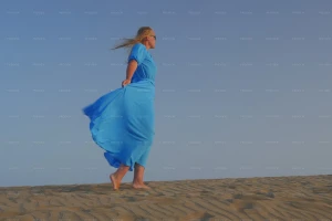 خانومی که لباس آبی پوشیده و در حال قدم زدن در کویر است