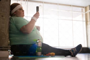 یک خانوم چاق در‌حال استراحت و استفاده از موبایل خود بعد از ورزش