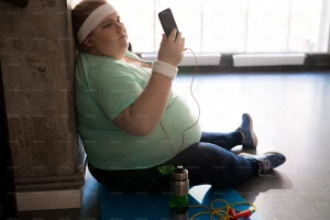 تصویر یک خانوم دارای اضافه وزن درحال استفاده از گوشی بعد از ورزش