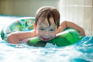 پسر کم سن درحال شنا در استخر با شناور