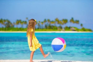 دختر کوچک در حال بازی با توپ روی شن‌های ساحل
