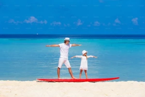 پدر و دختر در حال تمرین موج سواری در ساحل