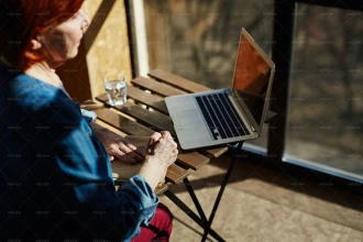 زن میانسال که در کنار یک میز و لپ تاپ نشسته است